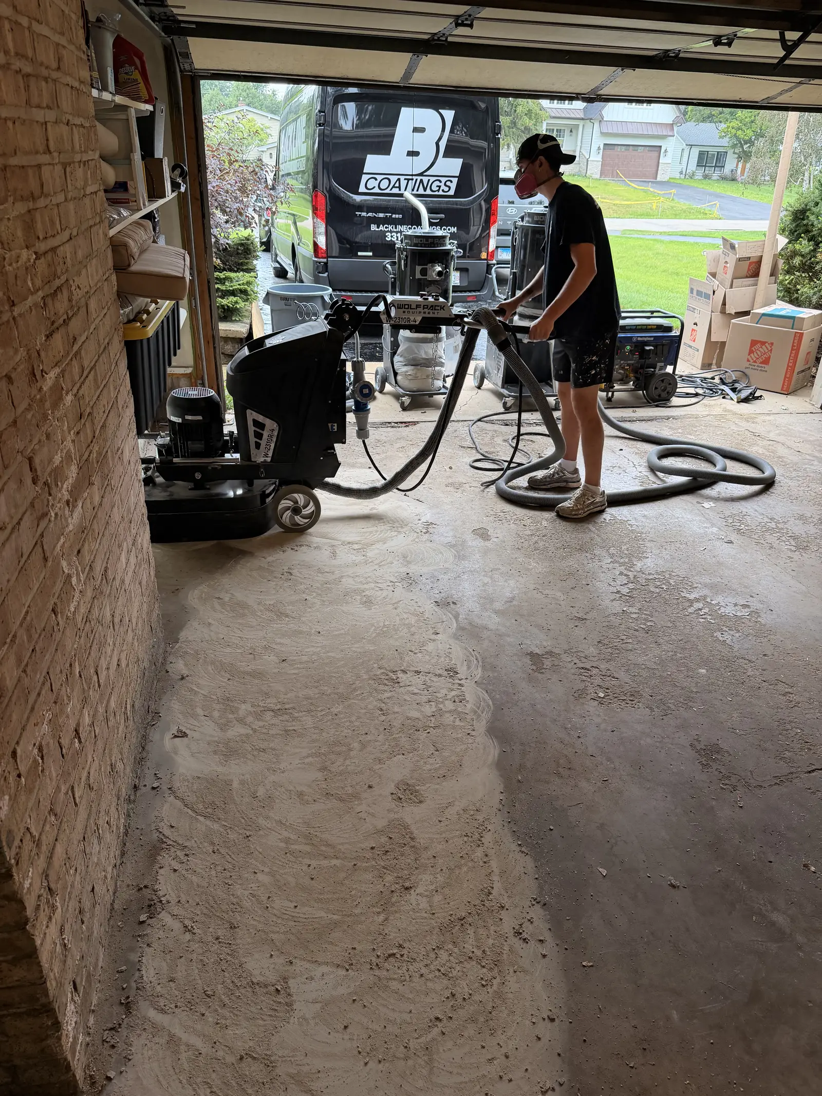 Blackline Coatings crew running a floor grinder across bare concrete in a garage